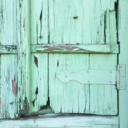 a photograph of the corner of a wooden door. it looks old and worn, and the entire thing has been painted over in chipped mint green paint.